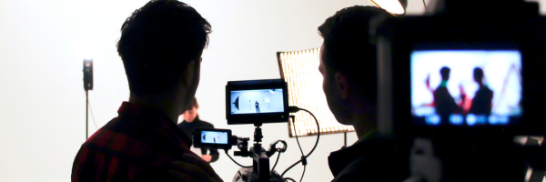 An image on a film set, two people looking at a monitor while a model or actor is in front of the lights